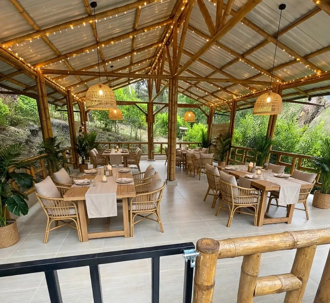 Long dining hall with teak tables and rattan chairs under string lights